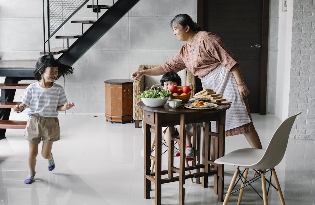 Happy elderly ethnic woman playing with running granddaughter before breakfast