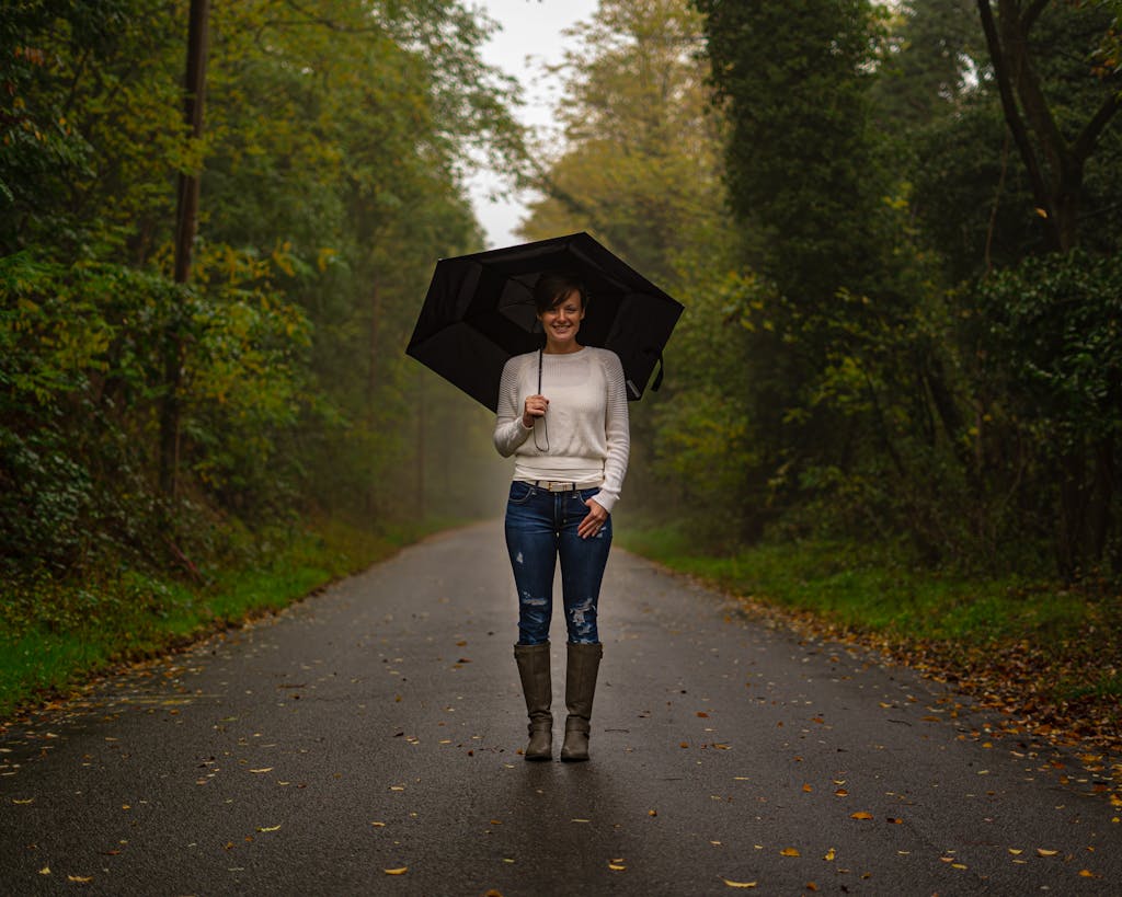 Woman in White Top and Blue Denim Jeans Holding Umbrella Walking on Road