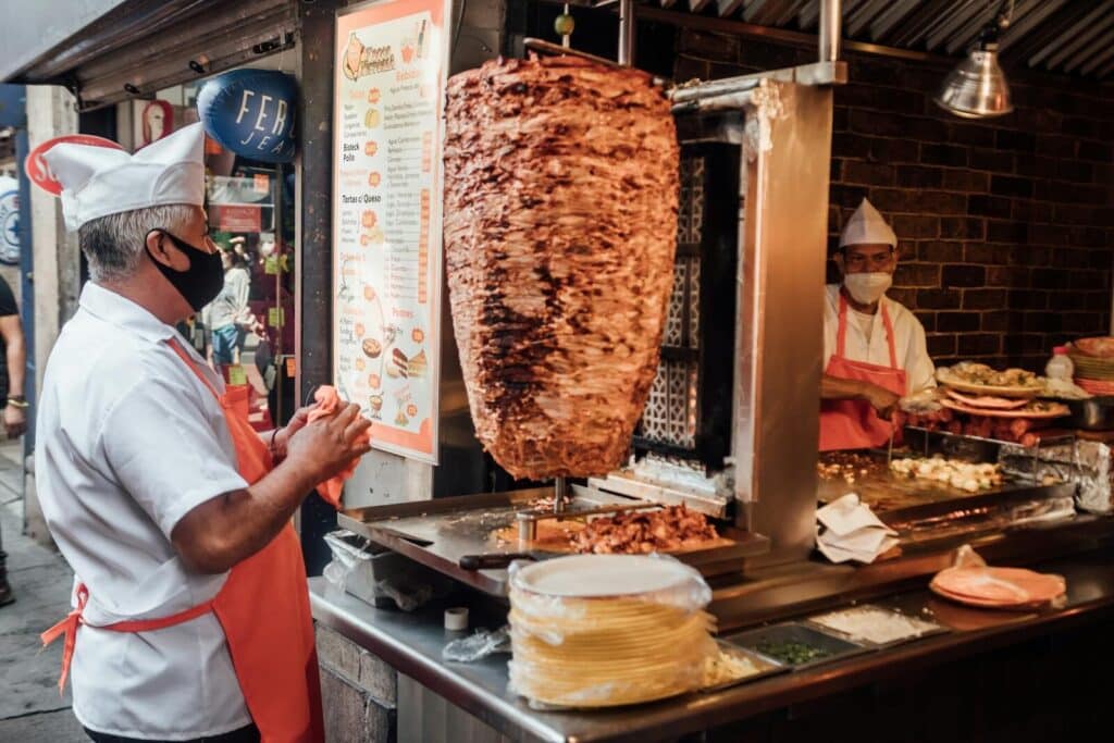 Tacos al pastor being prepared on a vertical spit at a street food stand in Mexico City