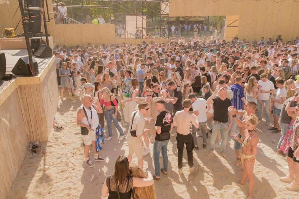 Crowd gathered at an outdoor beach-style event with music and fans