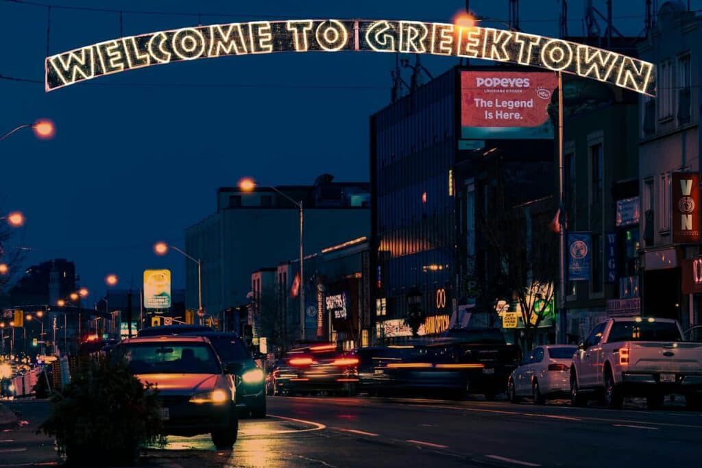 Greektown Toronto at night with the illuminated “Welcome to Greektown” sign and busy street