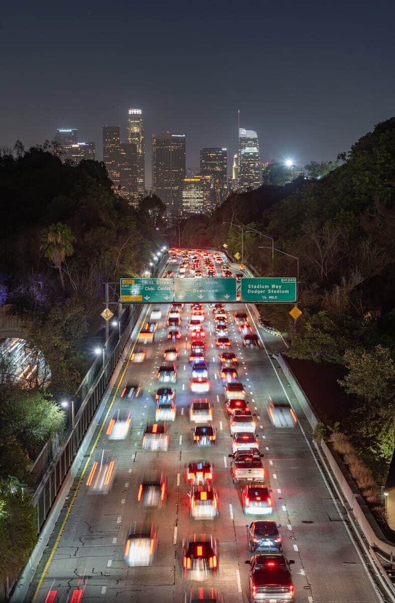 Busy Los Angeles freeway traffic at night with downtown skyline in the background, captured from above.