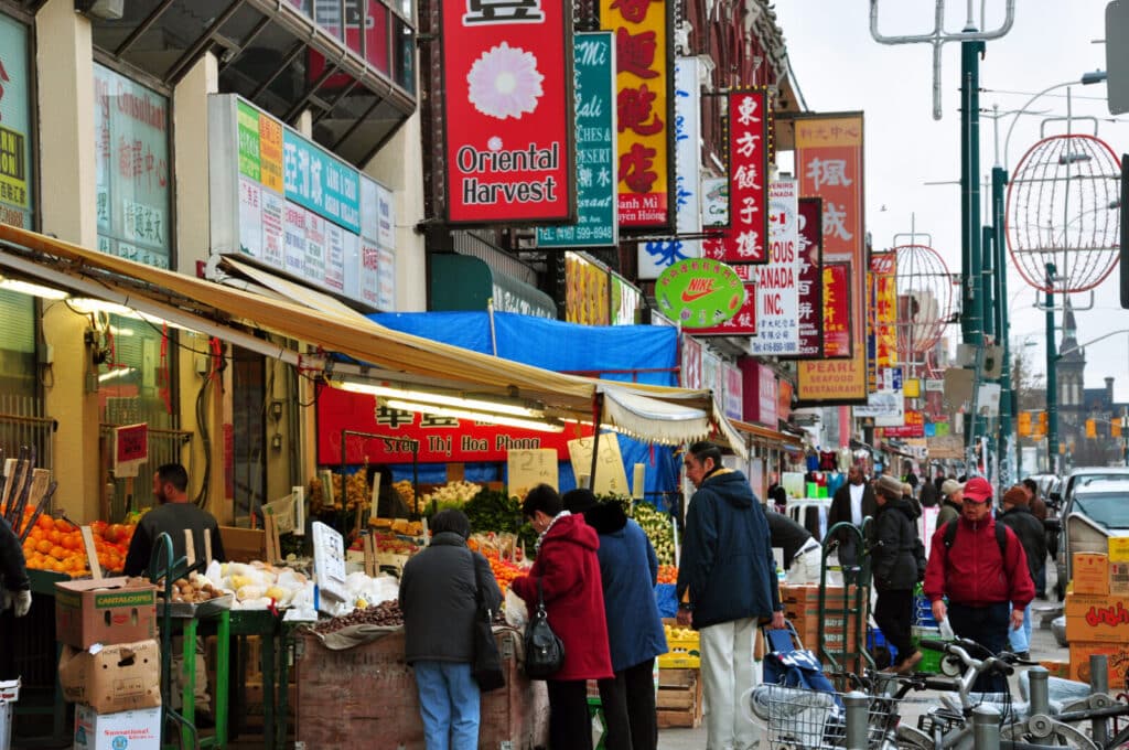 Chinatown Toronto street market with food stalls, shops, and people walking through a busy market street
