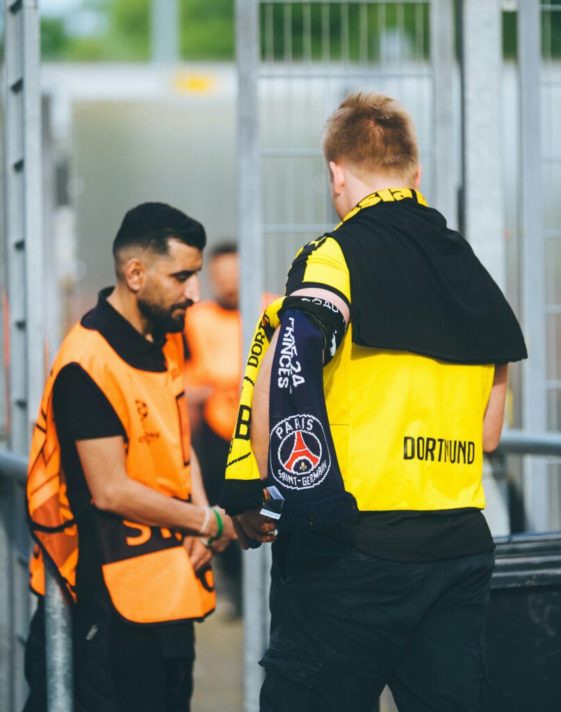 Security check at stadium entrance with staff inspecting fans before entry