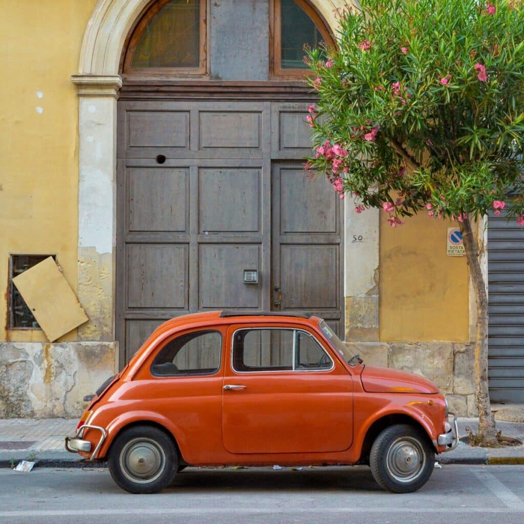 Small red car parked in front of traditional Italian building