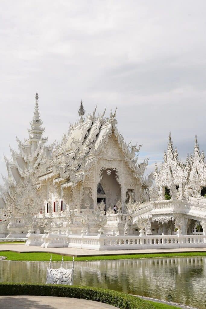 ornate white temple Wat Rong Khun in Chiang Rai reflected in a pond under a cloudy sky