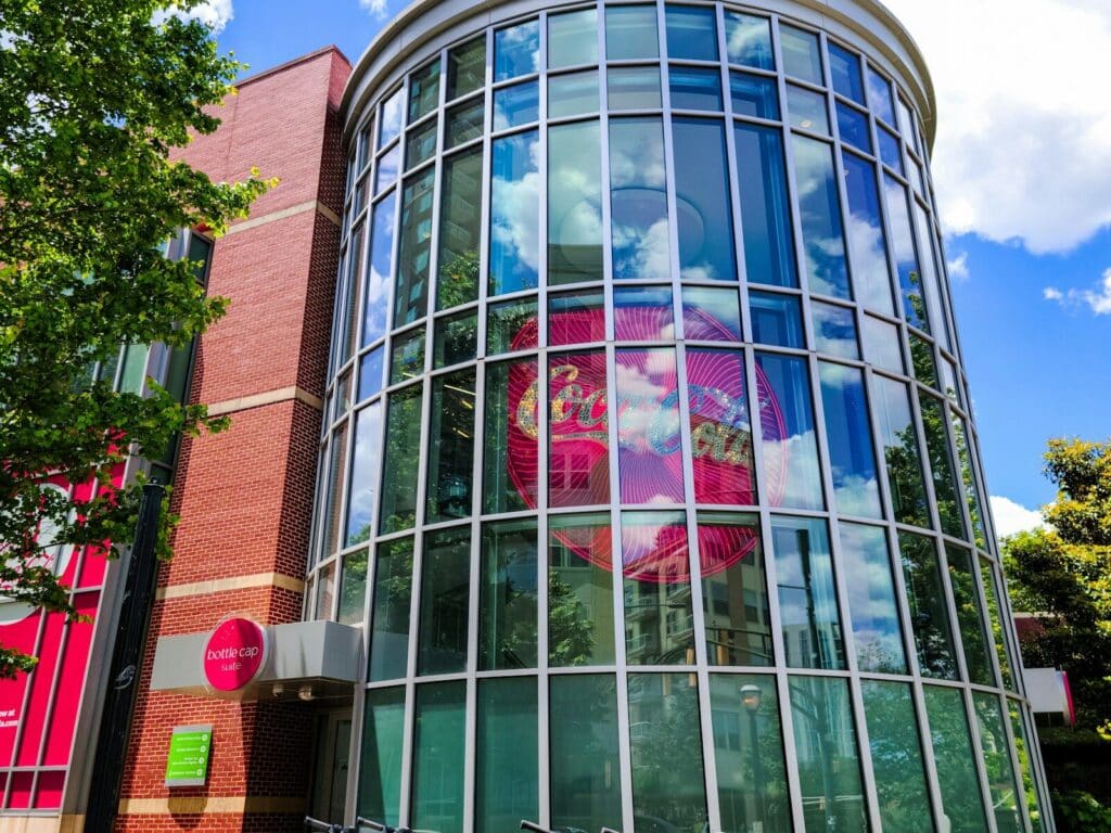 curved glass facade of the World of Coca-Cola museum in Atlanta with the Coca-Cola logo reflected inside