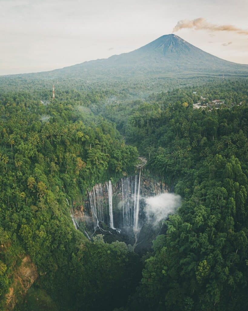 aerial view of Tumpak Sewu waterfall in Java with jungle and a volcanic peak in the background