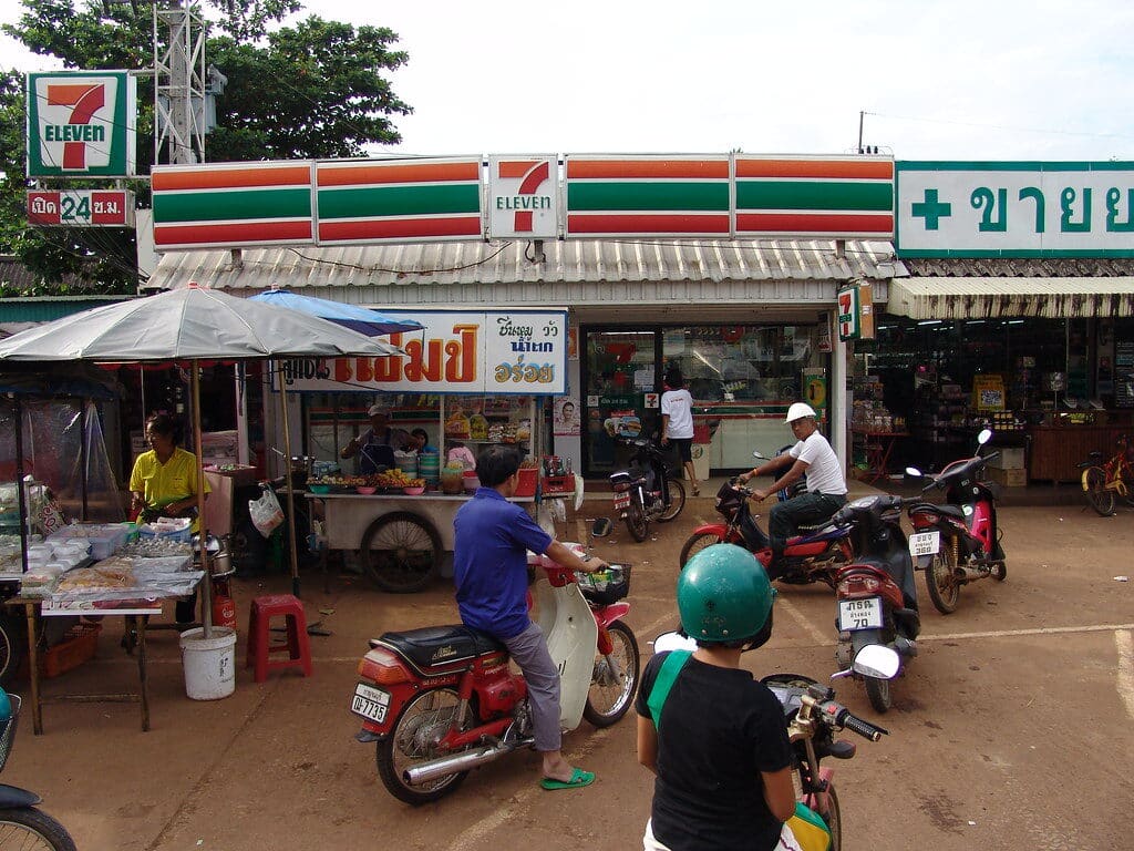 7-Eleven convenience store in Thailand with food stalls and motorbikes outside