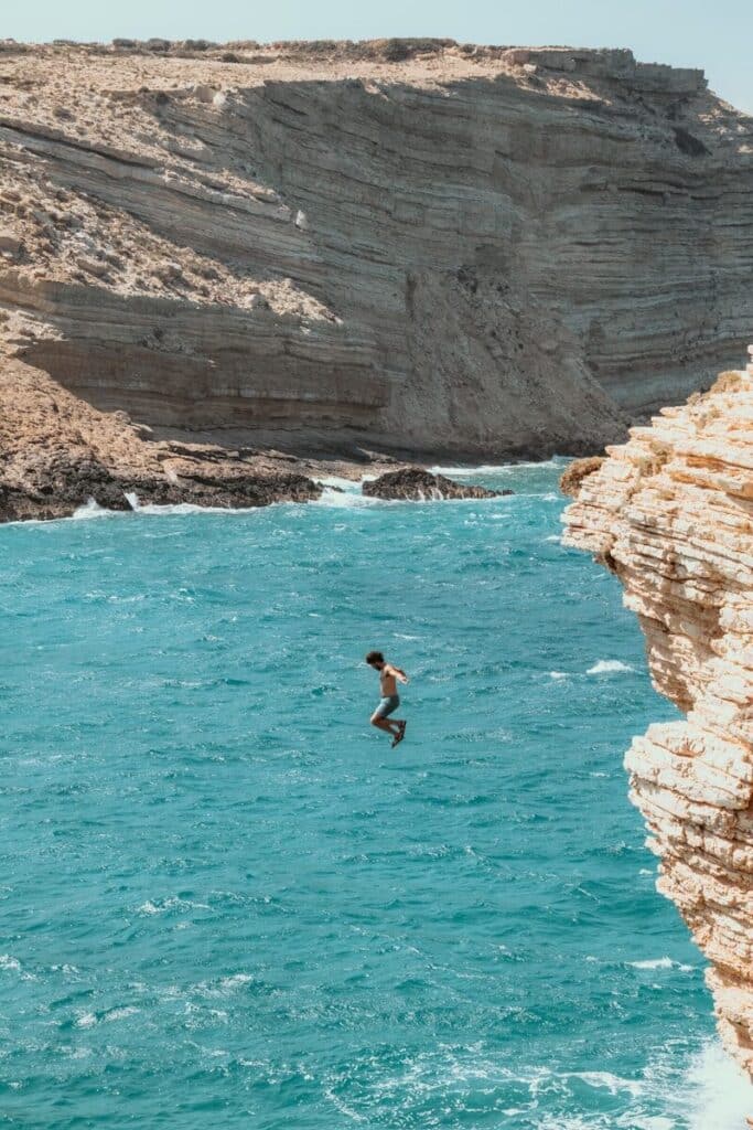 person jumping from a cliff into turquoise water between white limestone rocks on a Greek island