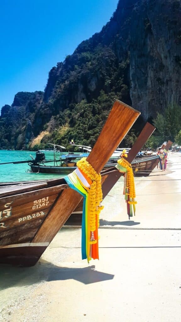 traditional Thai longtail boats decorated with garlands on a beach with turquoise water and cliffs