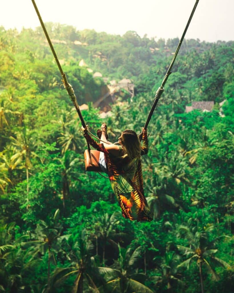 woman on a jungle swing above a lush green valley in Ubud Bali with palm trees below