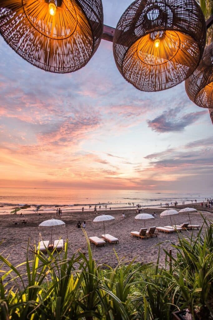 Bali beach at sunset with sun loungers and parasols viewed from a beach club with rattan lamps