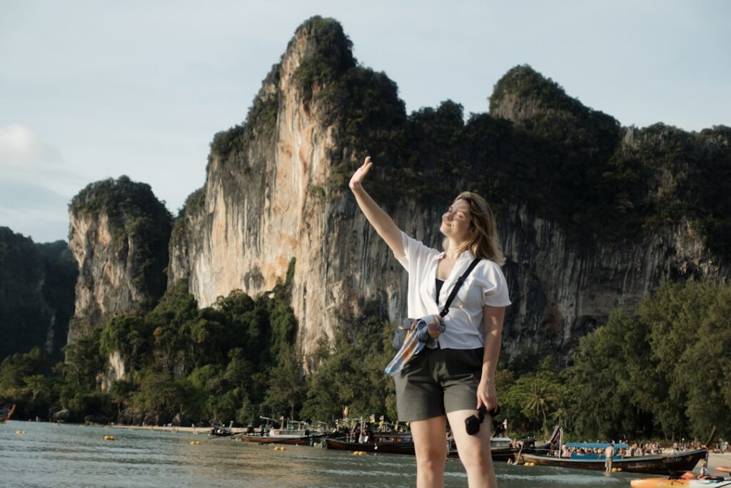 Woman raising her hand against dramatic cliffs by the sea, illustrating common mistakes travelling southeast asia