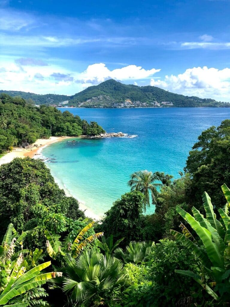 turquoise bay in Phuket surrounded by lush jungle and hills under a blue sky