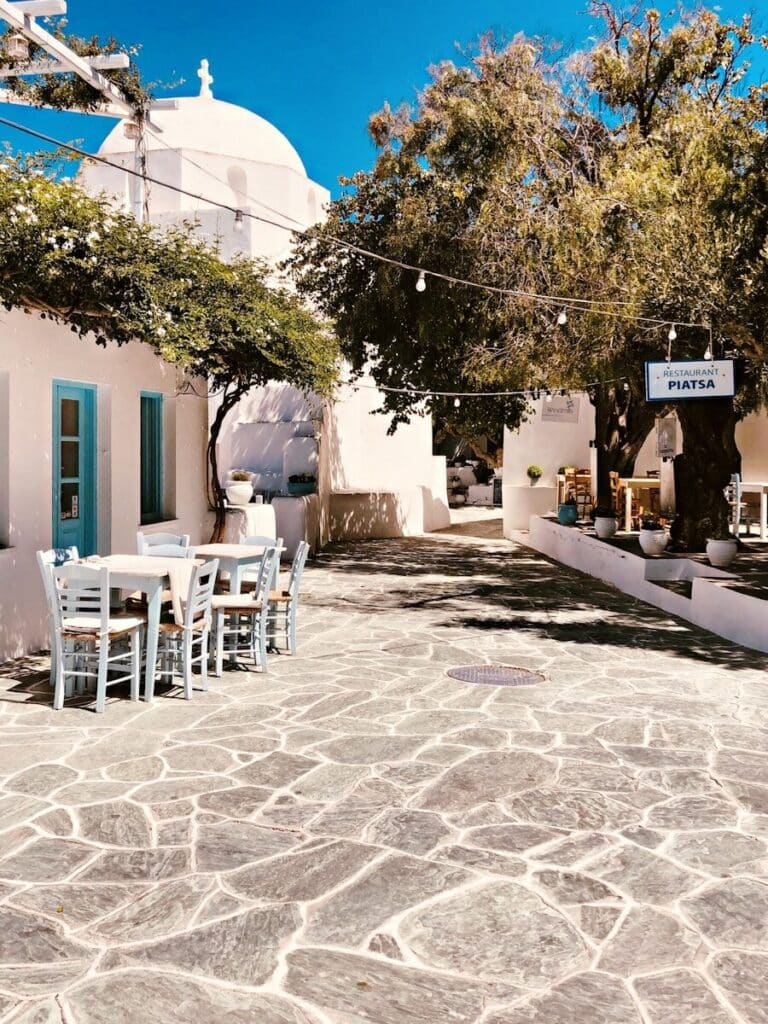 quiet village square in Folegandros with white church dome and taverna under olive trees