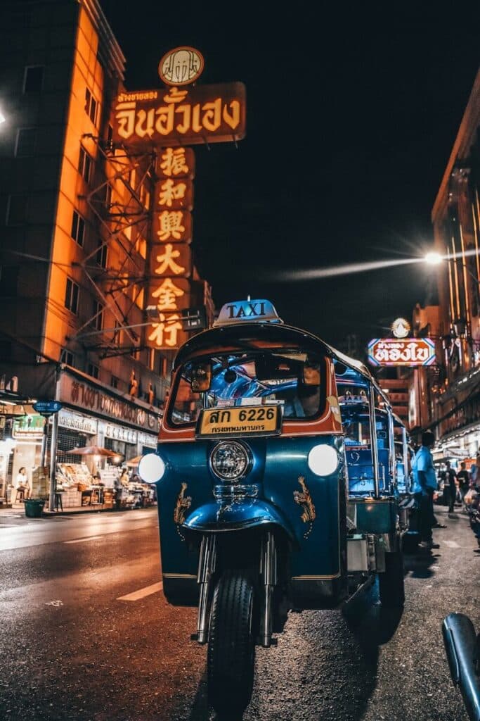 blue tuk-tuk on a busy Bangkok street at night with Chinese neon signs in the background