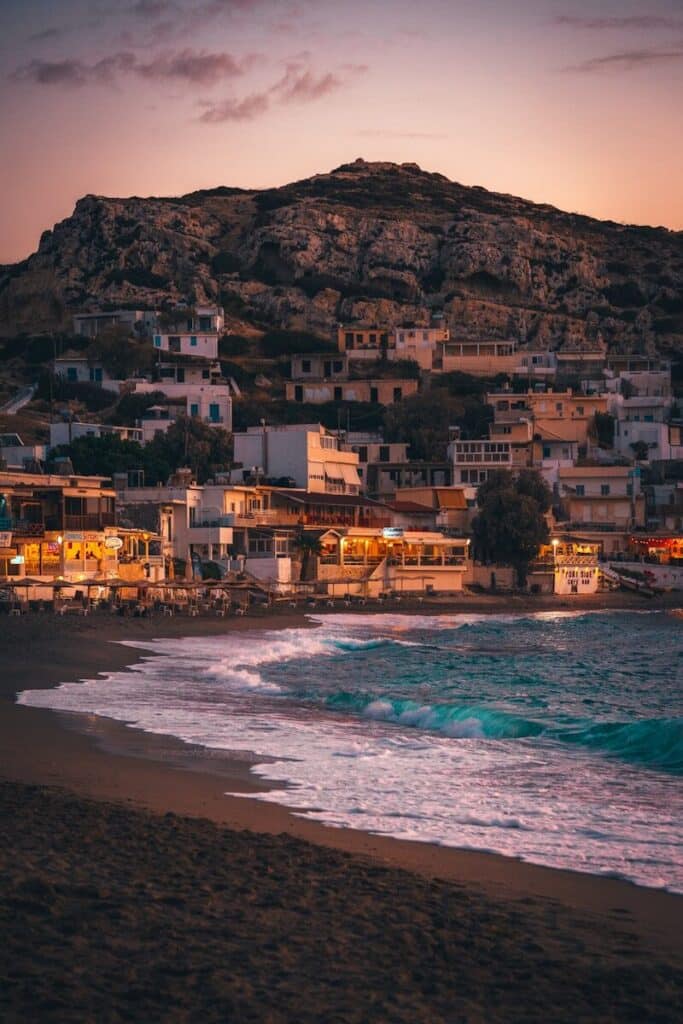 Crete coastal village at sunset with beach restaurants lit up and waves in the foreground