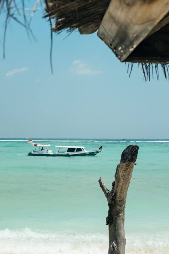 small white boat floating in shallow turquoise water off Gili Air with a thatched roof in the foreground