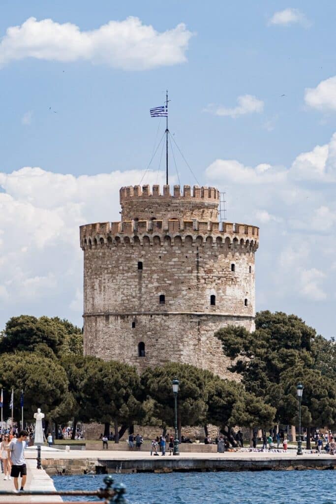 White Tower of Thessaloniki on the waterfront with Greek flag and blue sky