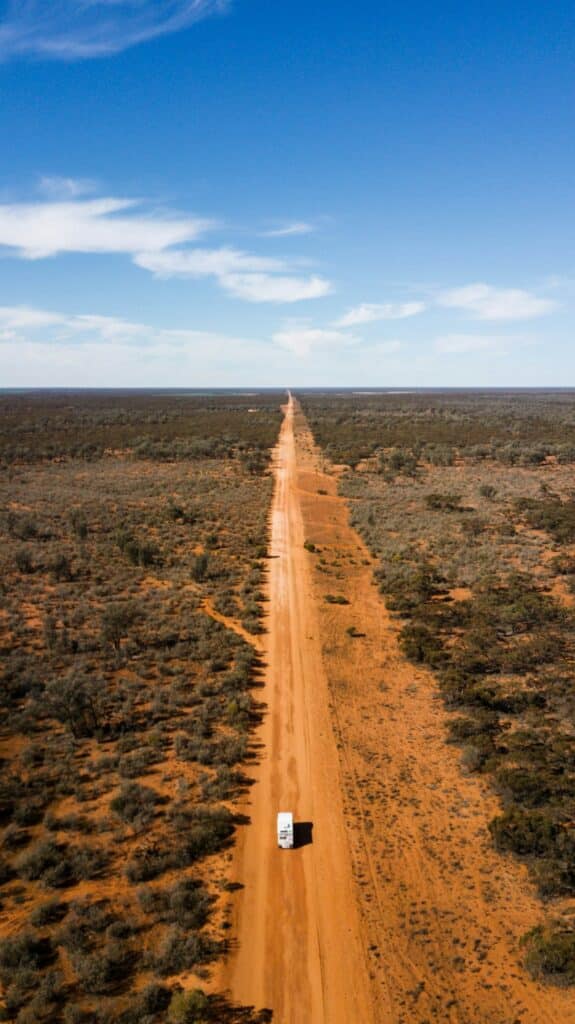 Dirt road through green grass fields under a blue sky