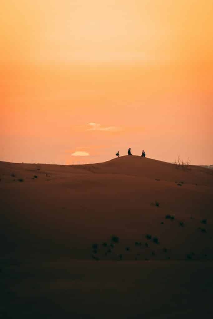 Travelers kneeling to watch a desert sunset near Dubai