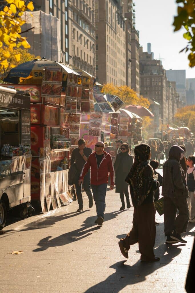 Travelers walking past food stalls on a sunny street