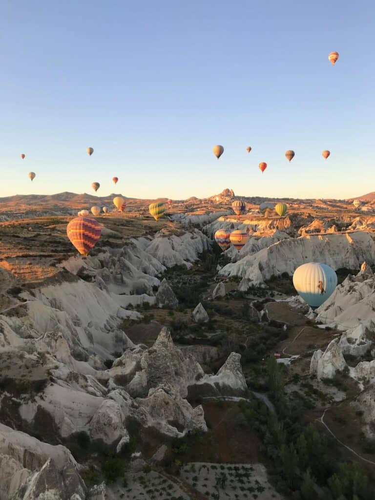 several hot air balloons flying over a Cappadocia valley